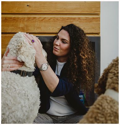 Esther Fischer sitzt im Profil an eine helle Wand gelehnt, in bequemer Kleidung mit orangenem Shirt und grauer Hose. Ihr Blick ist ruhig, fast meditativ, die Haltung entspannt – ein Moment der Einkehr und des Spürens. Diese Szene steht für die leisen, aber tief wirkenden Räume, die sie in ihrer Arbeit bei wirksam wachsen schafft: Nervensystemregulation, somatische Begleitung und bewusste Selbstführung für Frauen in Wandelprozessen und Führungsverantwortung.