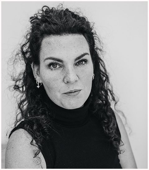 Esther Fischer im monochromen Porträt, mit ernstem, fokussiertem Blick direkt in die Kamera. Sie trägt ein schwarzes ärmelloses Rollkragen-Oberteil, ihr lockiges Haar ist teils hochgesteckt, die Struktur ihrer Haut ist deutlich sichtbar. Die Aufnahme vermittelt Klarheit, Tiefe und Entschlossenheit – ein starkes visuelles Statement für ihre Arbeit als Mentorin für Selbstführung, emotionale Entwicklung und Nervensystemarbeit bei wirksam wachsen, mit Sitz in Bergisch Gladbach.
